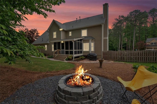 back of property featuring fence, an outdoor fire pit, a sunroom, a chimney, and a yard