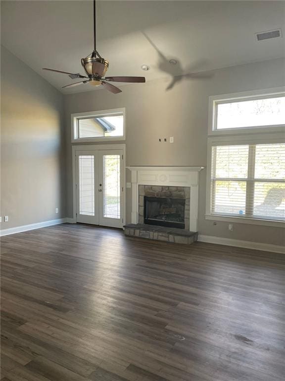 unfurnished living room featuring dark wood-style floors, baseboards, visible vents, and a stone fireplace