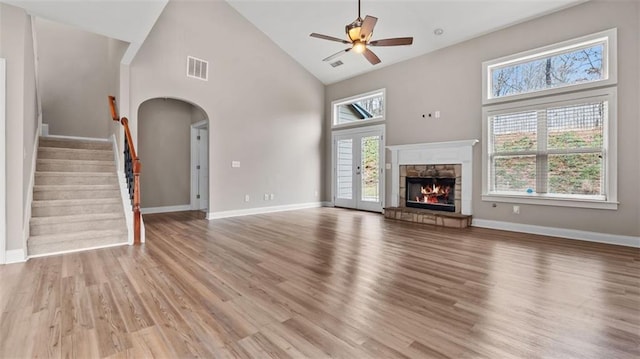 unfurnished living room with visible vents, high vaulted ceiling, stairway, light wood-style floors, and a fireplace