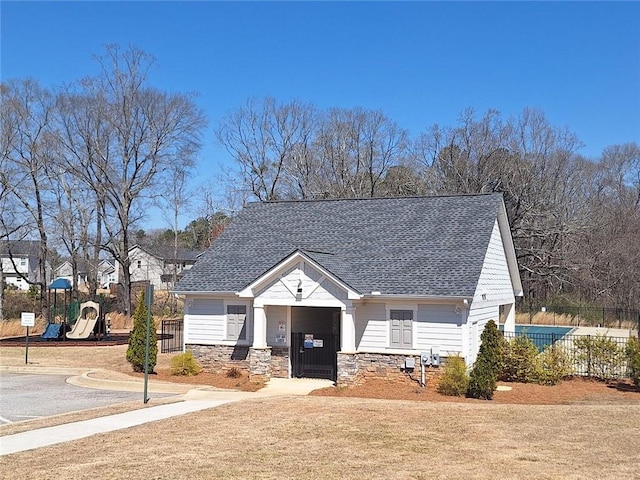 view of front of home featuring a playground, fence, stone siding, and a shingled roof