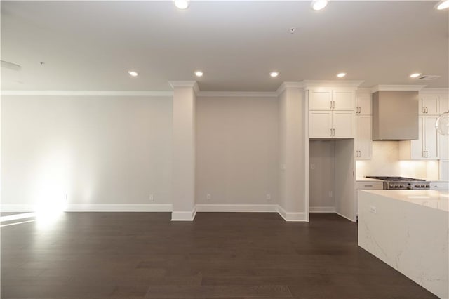 interior space featuring wall chimney range hood, white cabinetry, dark hardwood / wood-style floors, and ornamental molding