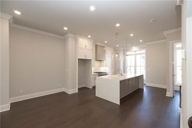 kitchen featuring dark wood-type flooring, a center island with sink, sink, hanging light fixtures, and white cabinetry