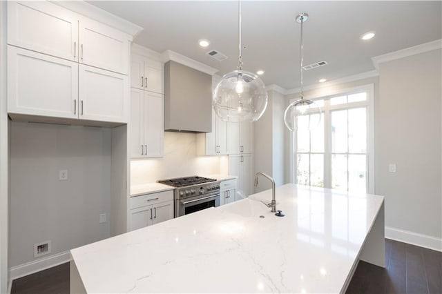 kitchen with light stone countertops, high end stove, an island with sink, decorative light fixtures, and white cabinets