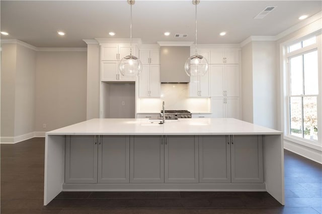 kitchen with a large island with sink, white cabinets, a healthy amount of sunlight, and decorative light fixtures