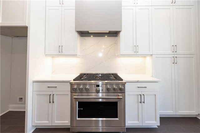 kitchen with high end stove, tasteful backsplash, white cabinetry, and wall chimney exhaust hood