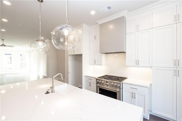 kitchen with sink, hanging light fixtures, high end stainless steel range, light stone countertops, and white cabinetry