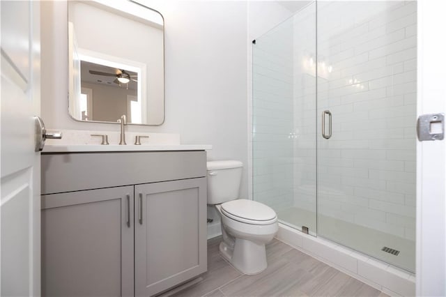 bathroom with ceiling fan, vanity, a shower with shower door, and toilet