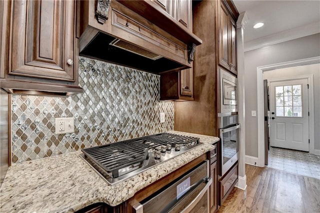 10020 Normandy Ln, Suwanee, GA 30024 - kitchen with custom exhaust hood, appliances with stainless steel finishes, light stone counters, decorative backsplash, and crown molding