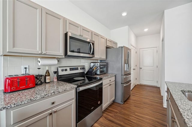 kitchen with gray cabinets, dark hardwood / wood-style flooring, stainless steel appliances, light stone countertops, and backsplash