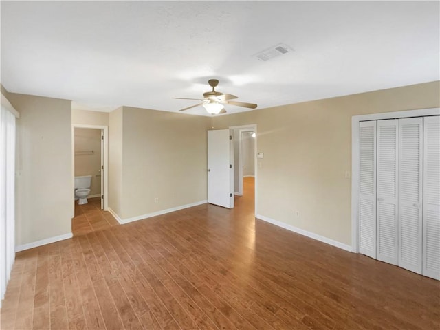 unfurnished bedroom featuring ceiling fan, ensuite bath, hardwood / wood-style floors, and a closet