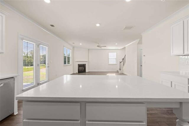 kitchen featuring white cabinets, ornamental molding, a center island, dishwasher, and a glass covered fireplace