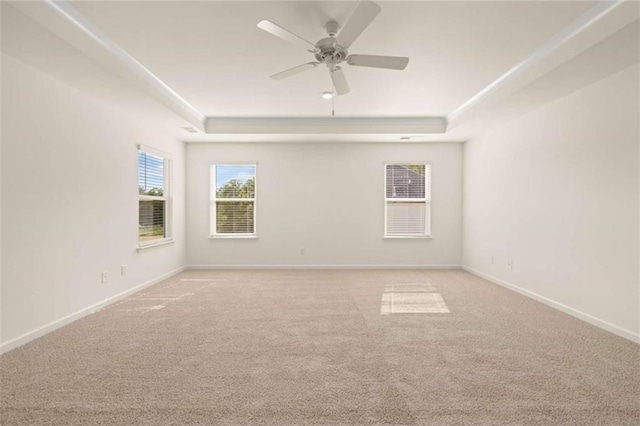 empty room with light carpet, ceiling fan, baseboards, and a raised ceiling