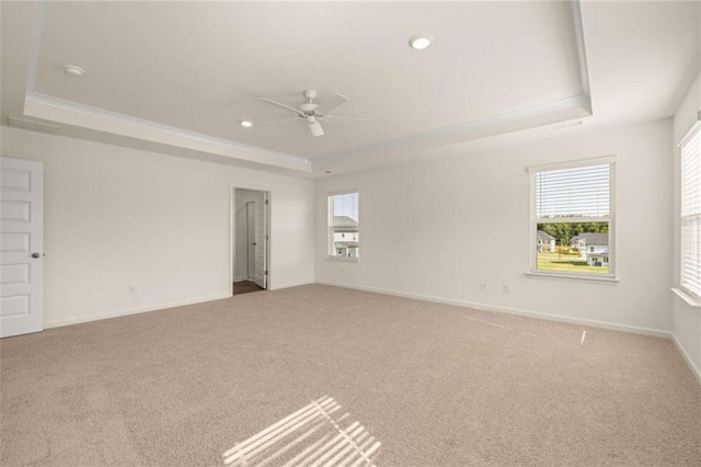 empty room featuring a ceiling fan, a tray ceiling, light colored carpet, and baseboards