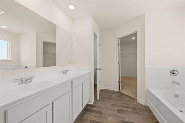 full bathroom with a walk in closet, a garden tub, a sink, and wood tiled floor