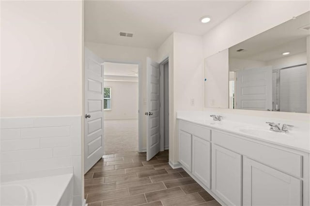 bathroom featuring double vanity, visible vents, a garden tub, wood tiled floor, and a sink