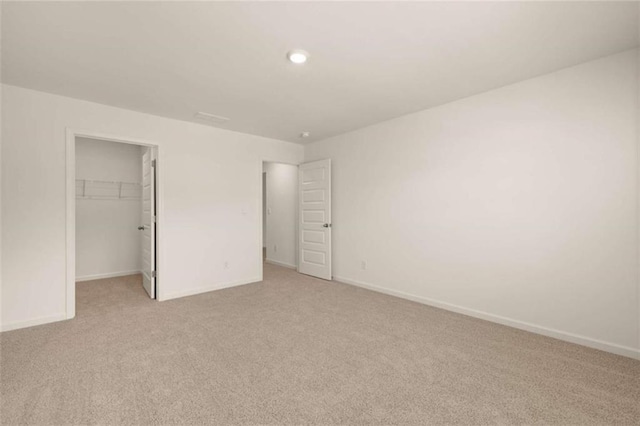 unfurnished bedroom featuring a spacious closet, baseboards, a closet, and light colored carpet