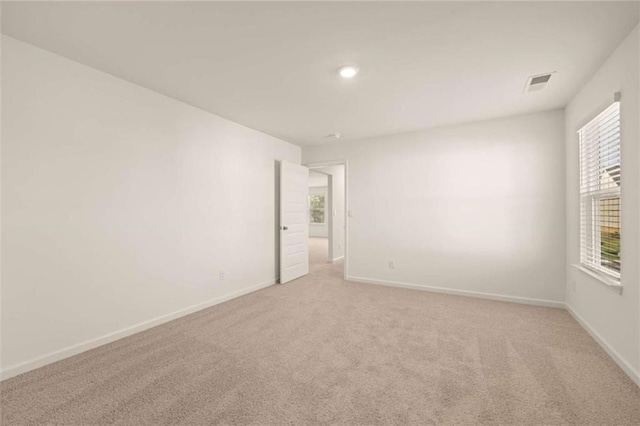 spare room featuring light carpet, visible vents, and baseboards