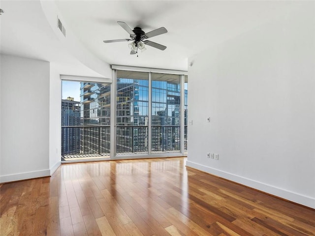 empty room featuring hardwood / wood-style floors, a wall of windows, and ceiling fan