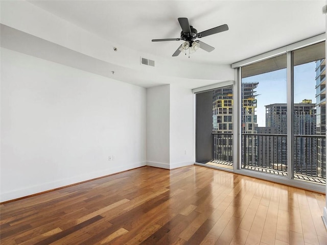 unfurnished room with wood-type flooring, ceiling fan, and a wall of windows