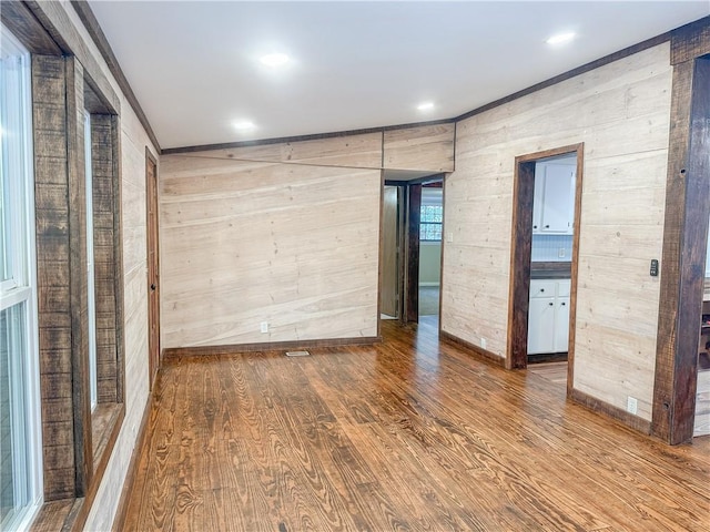 unfurnished room with baseboards, wood walls, wood finished floors, and ornamental molding