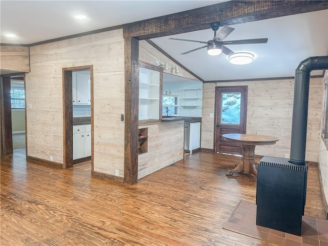 interior space featuring a wood stove, ceiling fan, plenty of natural light, wood finished floors, and vaulted ceiling with beams