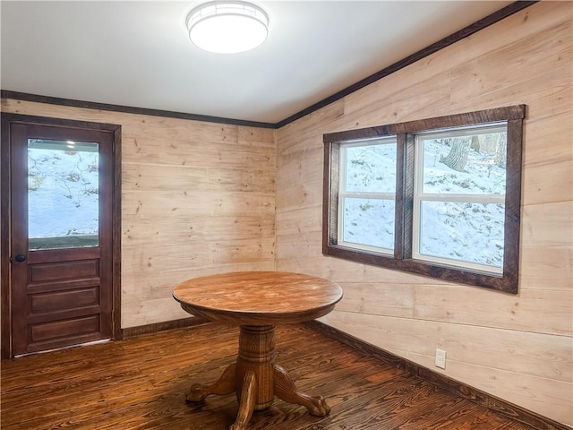 dining room with baseboards, wood walls, dark wood-style flooring, and crown molding