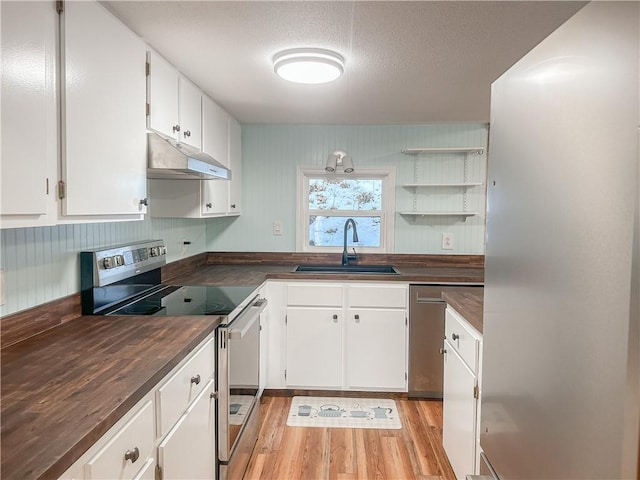 kitchen with stainless steel appliances, under cabinet range hood, dark countertops, a sink, and white cabinetry