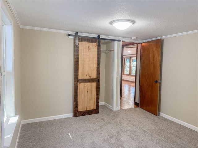 unfurnished bedroom with a textured ceiling, crown molding, a barn door, a closet, and carpet floors