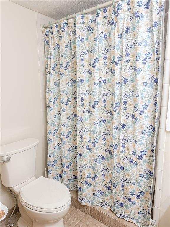 bathroom featuring toilet, a shower with shower curtain, and tile patterned flooring