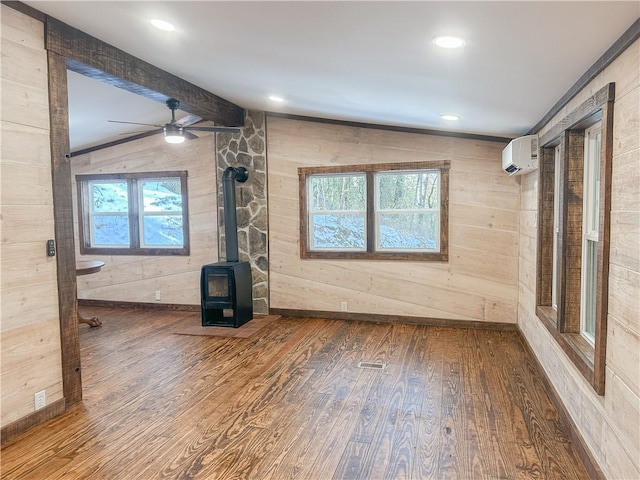 unfurnished living room with a wood stove, ceiling fan, a wealth of natural light, and wood finished floors