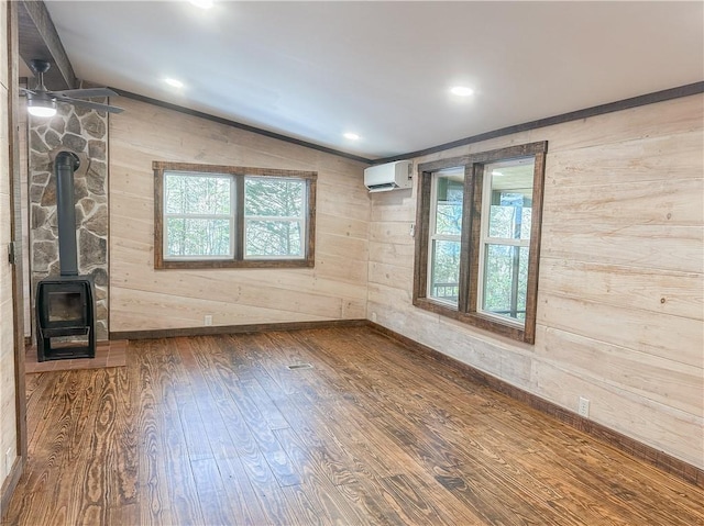 unfurnished living room featuring wood finished floors, a healthy amount of sunlight, a wall mounted air conditioner, and a wood stove