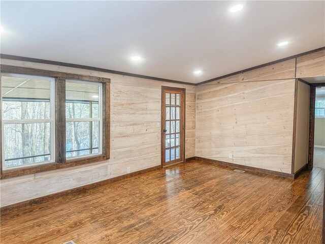 spare room featuring baseboards, wood finished floors, crown molding, and plenty of natural light