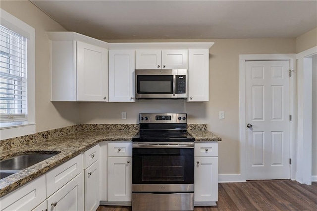 kitchen featuring appliances with stainless steel finishes, dark hardwood / wood-style flooring, dark stone counters, and white cabinets