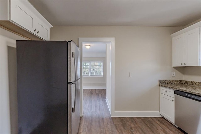 kitchen with stainless steel appliances, light stone countertops, white cabinets, and hardwood / wood-style floors