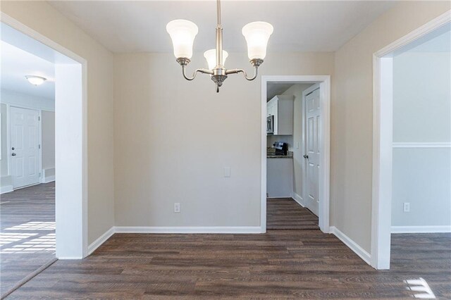 unfurnished dining area with dark wood-type flooring and an inviting chandelier