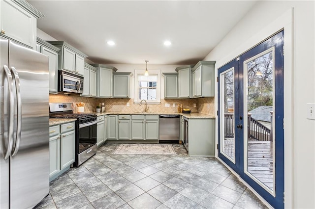 kitchen with pendant lighting, sink, appliances with stainless steel finishes, light stone counters, and french doors