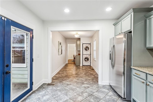 kitchen with stainless steel fridge, light stone countertops, and stacked washer / dryer