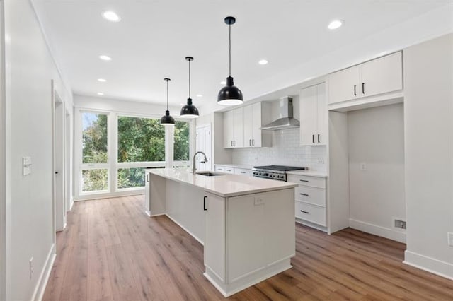 kitchen featuring white cabinets, a center island with sink, sink, hanging light fixtures, and wall chimney exhaust hood