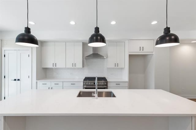 kitchen featuring white cabinetry, sink, wall chimney range hood, pendant lighting, and a kitchen island with sink