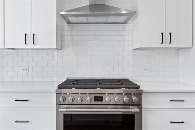 kitchen featuring high end range, white cabinets, tasteful backsplash, and wall chimney exhaust hood