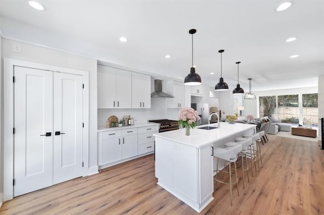 kitchen with a kitchen island with sink, sink, wall chimney exhaust hood, decorative backsplash, and white cabinetry