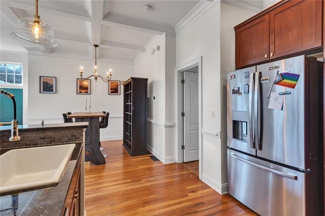 kitchen featuring light wood finished floors, stainless steel fridge, coffered ceiling, decorative light fixtures, and a sink
