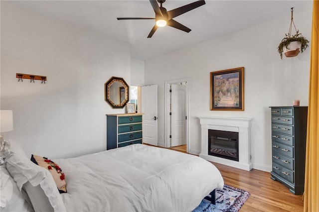 bedroom with baseboards, ceiling fan, a glass covered fireplace, and light wood-style floors