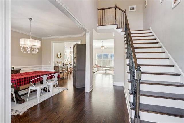 foyer with dark wood-style floors, ornamental molding, stairway, and ceiling fan with notable chandelier