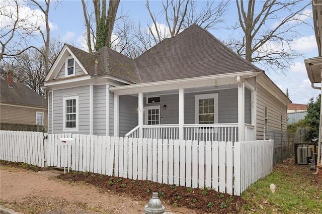 view of front of property featuring covered porch, a shingled roof, fence, and central AC