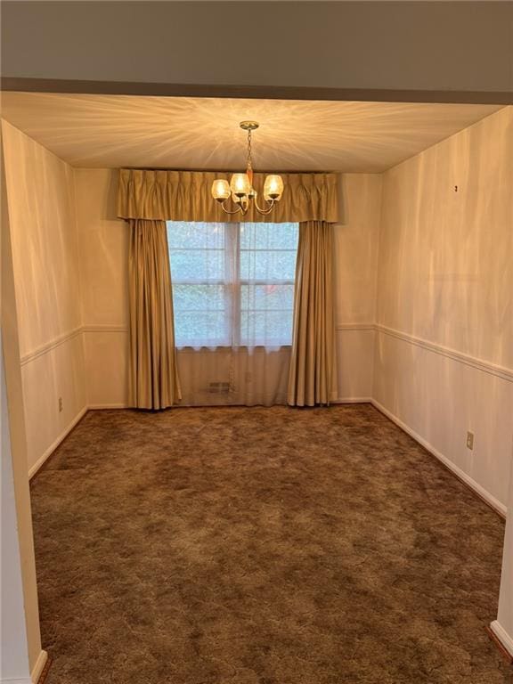 carpeted spare room with an inviting chandelier