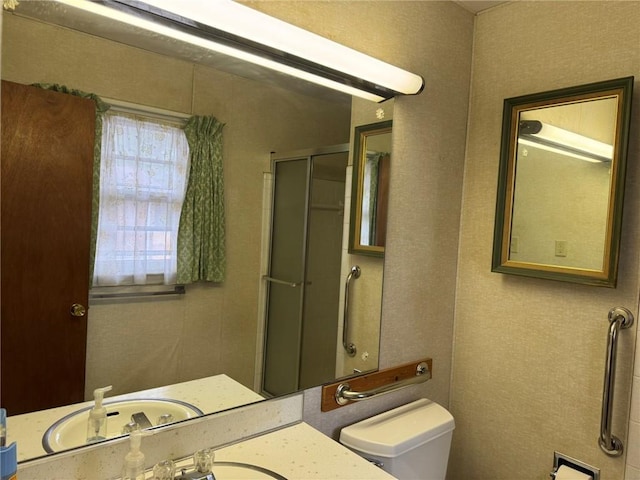 bathroom featuring a shower with door, sink, and toilet