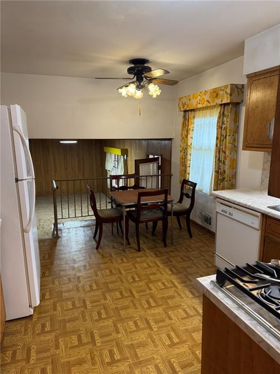 kitchen with light parquet flooring, wooden walls, ceiling fan, and white appliances