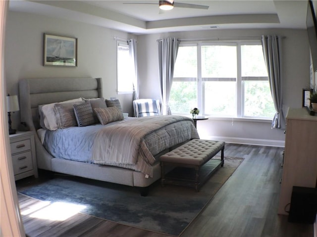 bedroom featuring dark wood-style flooring, baseboards, ceiling fan, and a raised ceiling