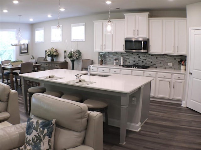kitchen with black cooktop, light countertops, dark wood finished floors, stainless steel microwave, and open floor plan